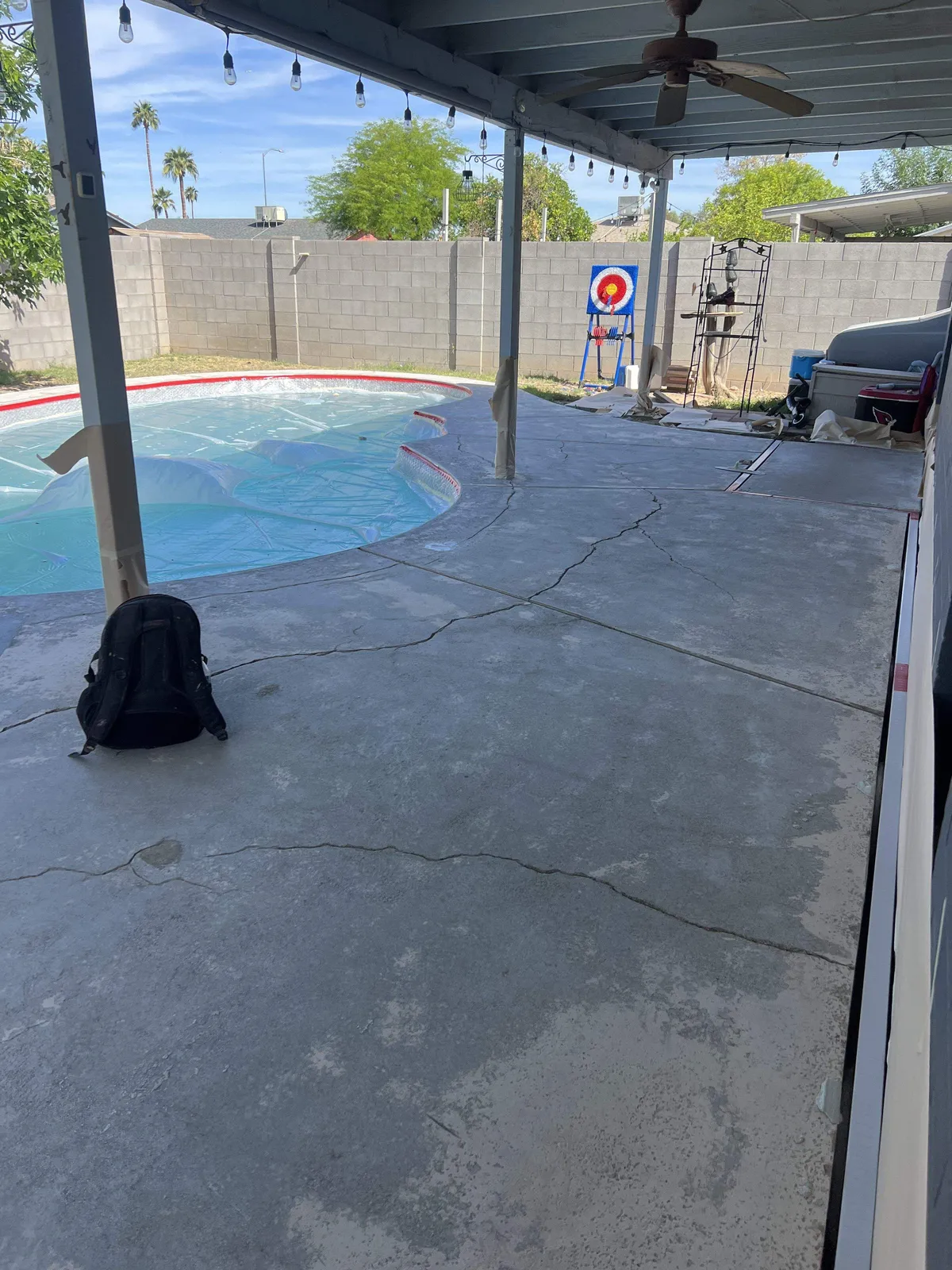 Pool deck with spider cracks across gray concrete before repair, under covered patio