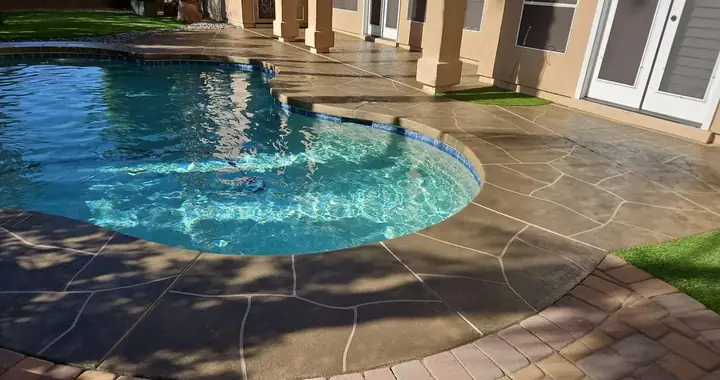 Dark brown flagstone coating around a curved pool, framed by a paver border