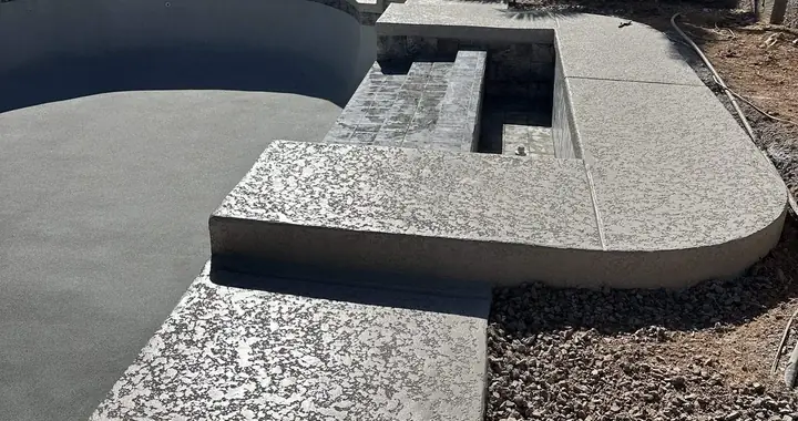 Rebuilt spa with a tiled spillway and fresh gray lace-texture coping and deck