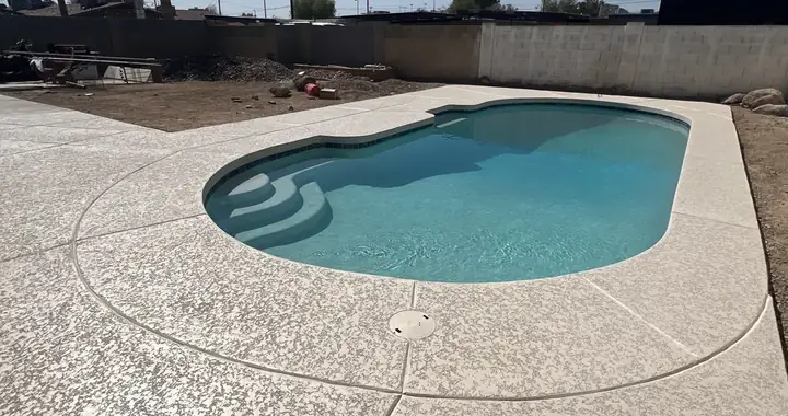Cream textured deck around a radius pool with entry steps and a deck drain