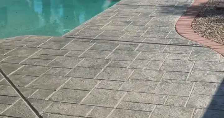 Gray stamped stone pattern with a red brick border along a pool